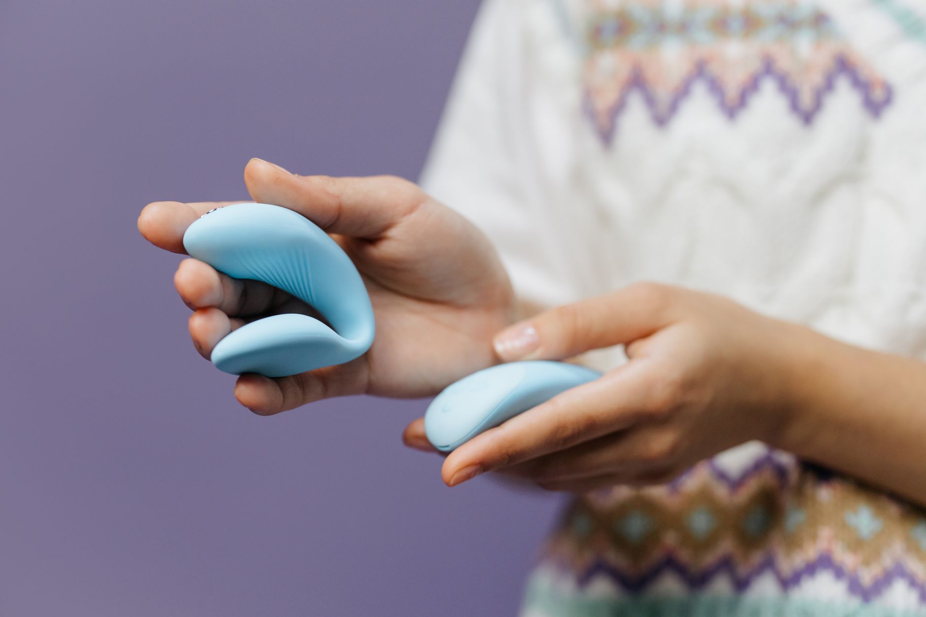 Woman holding blue and pink silicone vibrators, considering which tool to use for sensation
