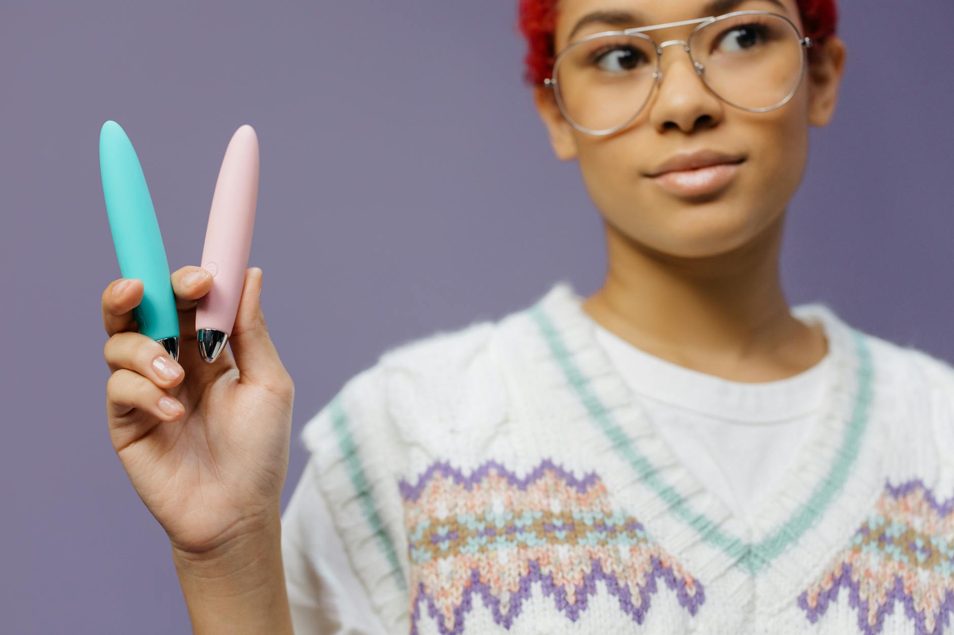 Woman holding two colorful vibrators against purple background