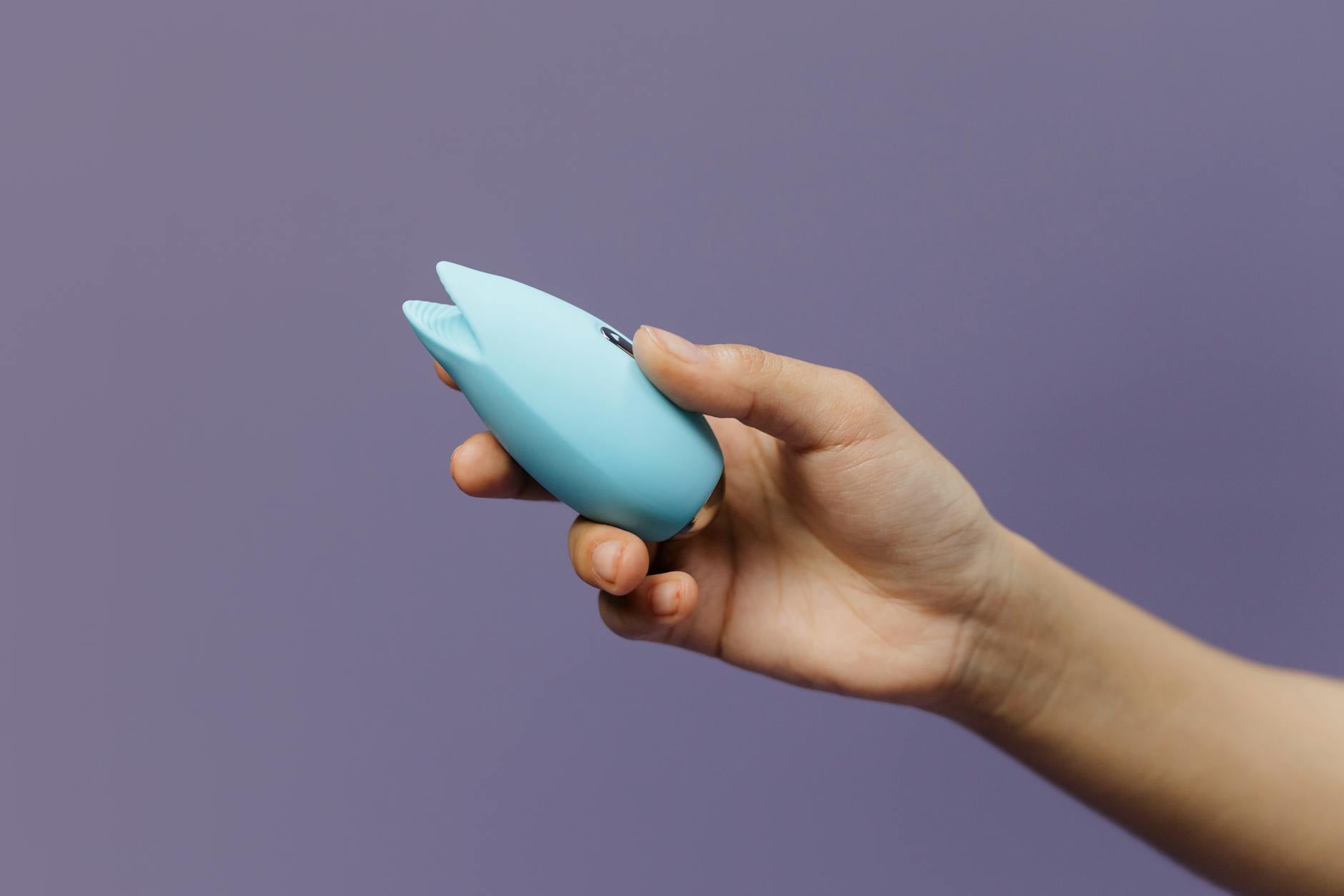 A silicone vibrator held in hand against a purple background, symbolizing self-pleasure and body connection.