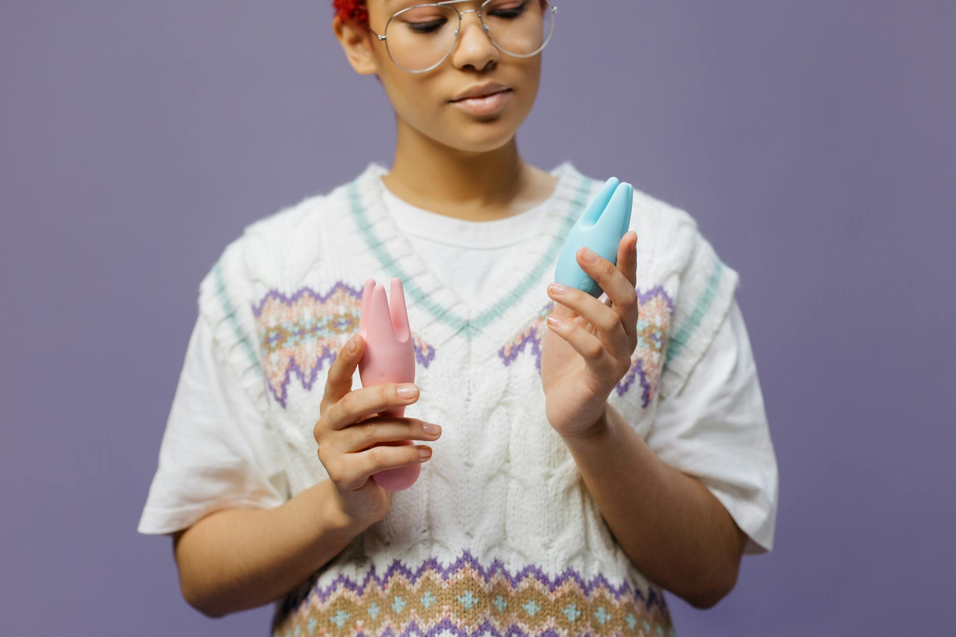 Close-up of hands holding a blue clitoral massager against a knitted sweater, representing reclaiming personal pleasure
