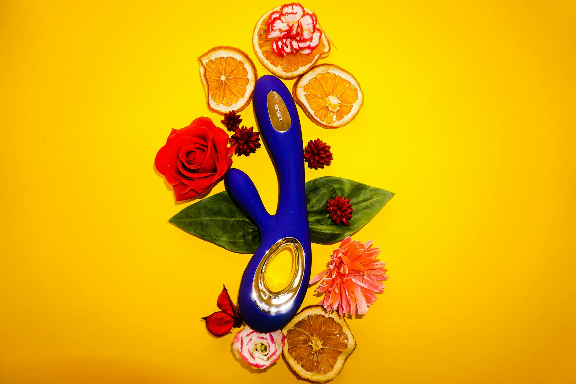 A blue lemon vibrator surrounded by flowers and orange slices on a yellow background.