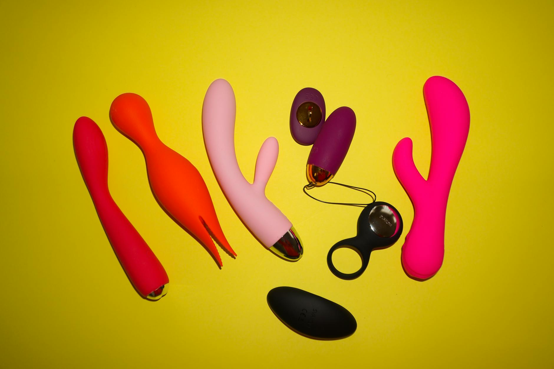 Colorful vibrators and intimate wellness tools arranged on a bright yellow surface